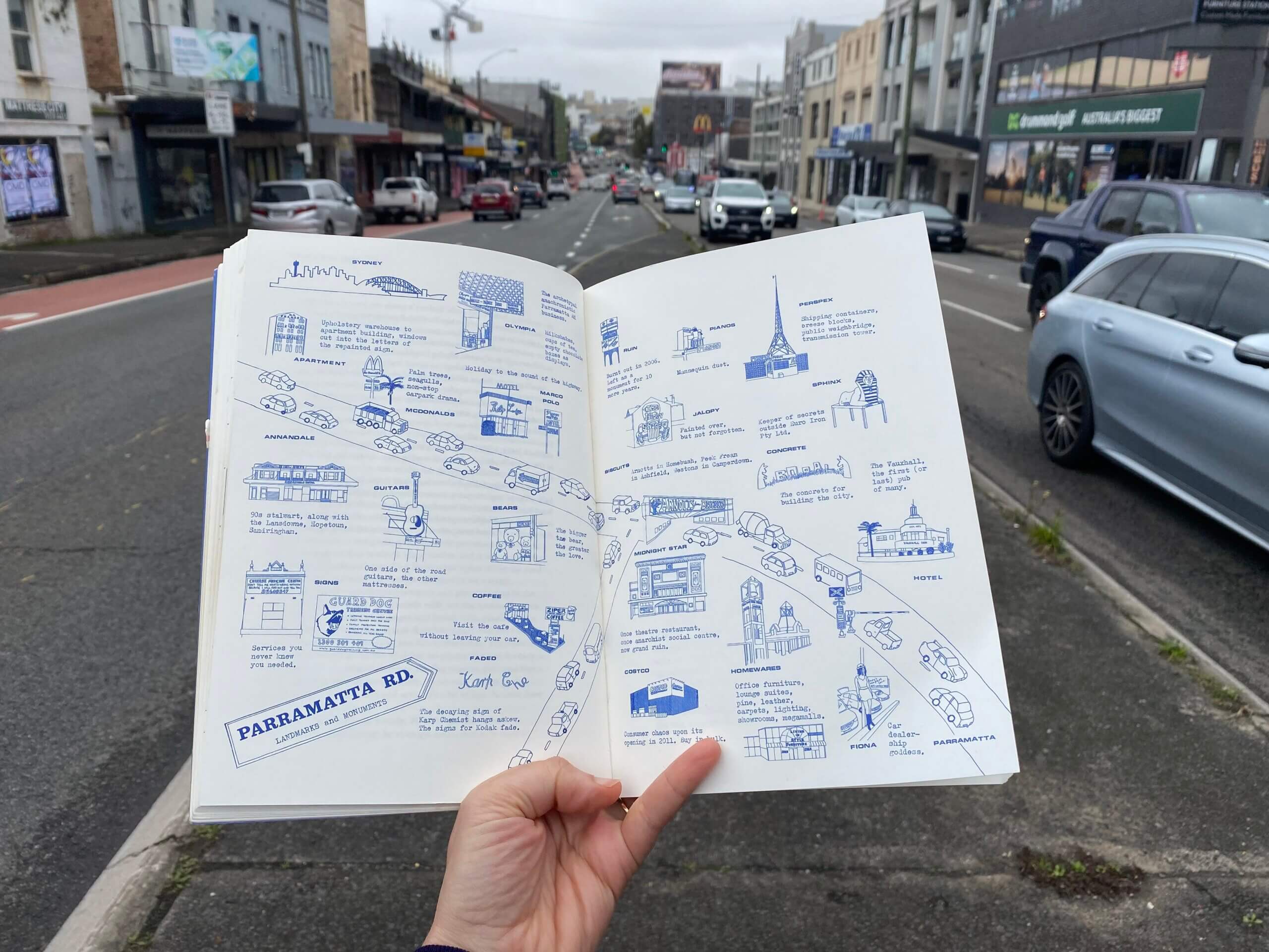 Photo of a hand holding an open book that contains an illustrated map of Parramatta Road